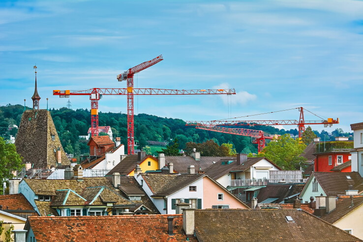 Les grues de chantier et les immeubles d'habitation témoignent de l'activité de construction et de l'évolution des prix des terrains à bâtir en Suisse.