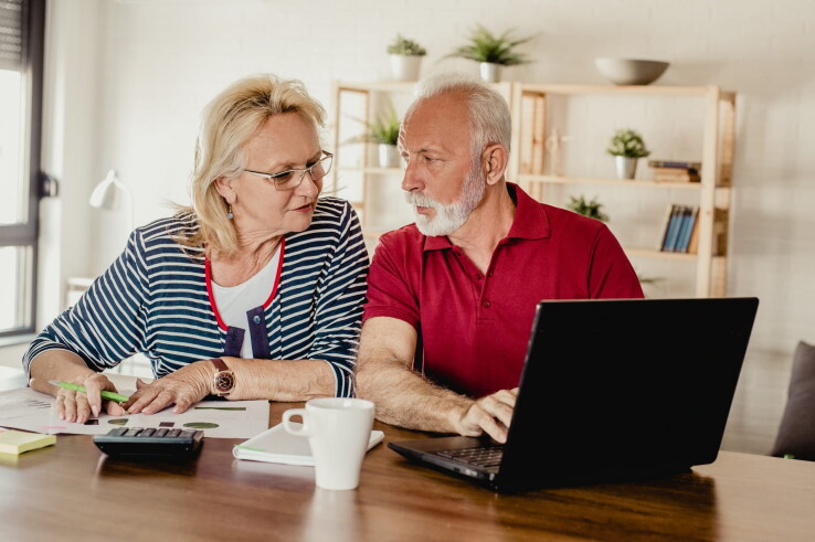 Un couple de personnes âgées compare sur son ordinateur portable les coûts d'achat et de fonctionnement d'une pompe à chaleur.