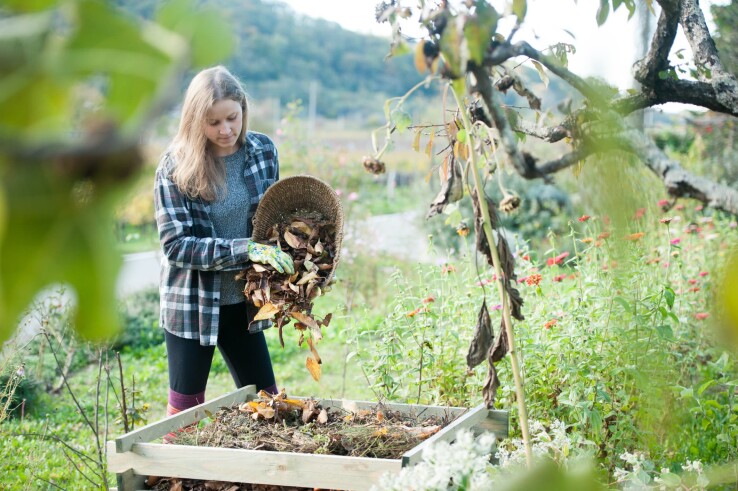 Eine Frau gibt Laub und Gartenabfälle auf einen Komposthaufen im Garten.