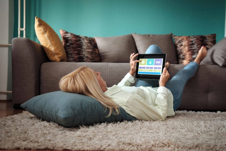Une personne contrôle, depuis son salon, les systèmes domotiques et énergétiques de son logement à l'aide d'une tablette.