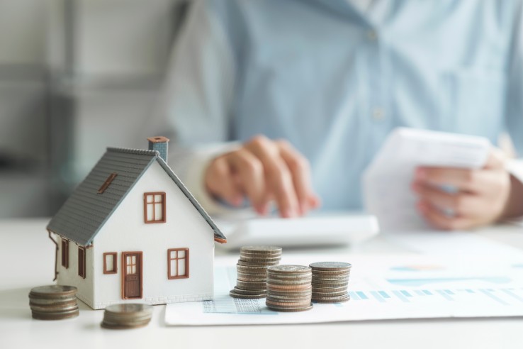Une maquette de maison et une pile de pièces de monnaie posées sur une table symbolisent les avantages financiers et les économies d'impôts liés à une rénovation énergétique.