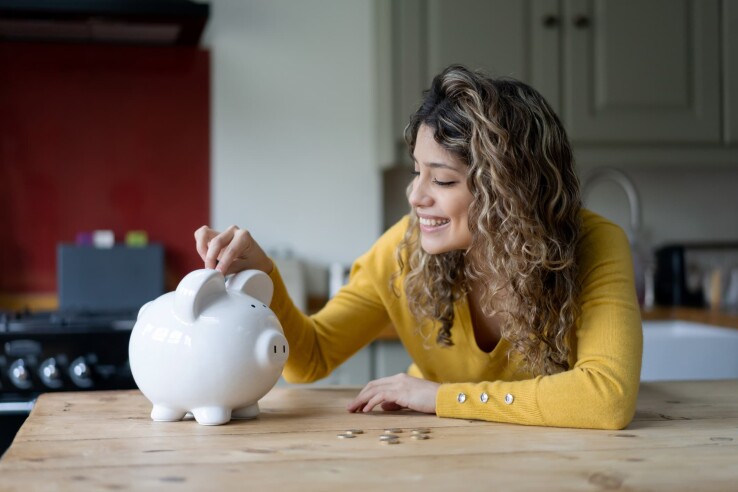 Une jeune femme met de l'argent dans une tirelire et prévoit d'économiser un apport personnel pour la construction d'une maison ou l'achat d'un logement.
