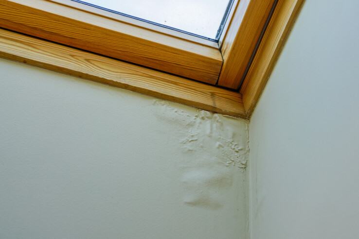 Des dégâts dus à l'humidité sur un mur situé sous une fenêtre de toit, à titre d'exemple de vice de construction.