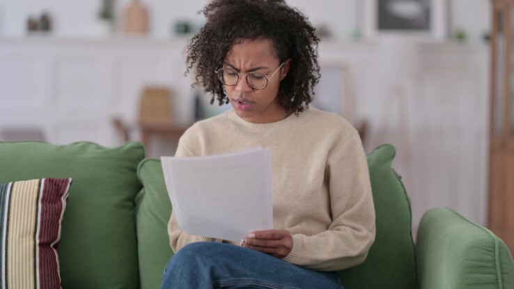 Une femme lit une lettre sur le canapé, image symbolique d'une augmentation de loyer annoncée.