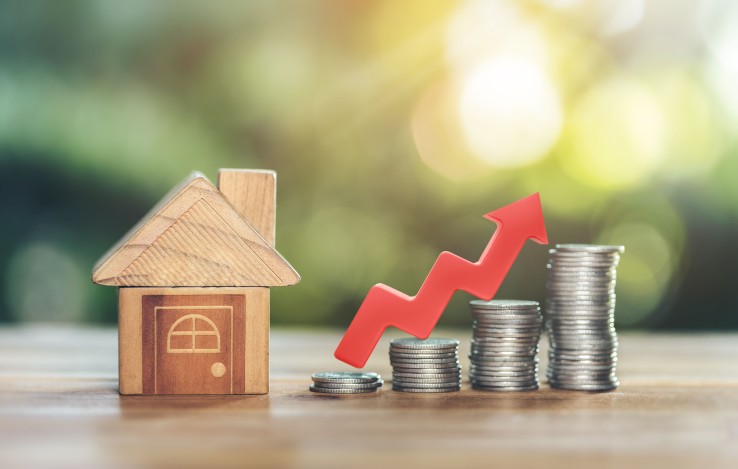 Maquette d'une maison en bois à côté de pièces de monnaie, symbole de la plus-value immobilière générée par la rénovation énergétique