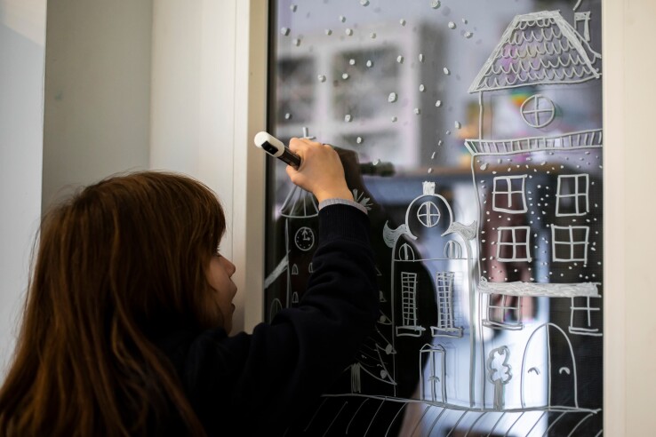 Fenêtre de l’Avent avec un décor hivernal de maisons dessiné sur la vitre au feutre craie.