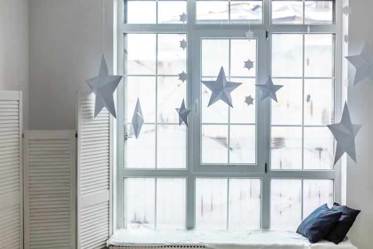 Fenêtre de l’Avent sobre décorée d’étoiles blanches en papier de différentes tailles.