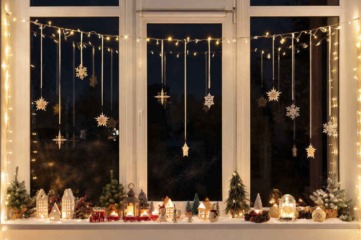 Fenêtre de l’Avent illuminée avec des étoiles suspendues et un village hivernal sur le rebord de la fenêtre.