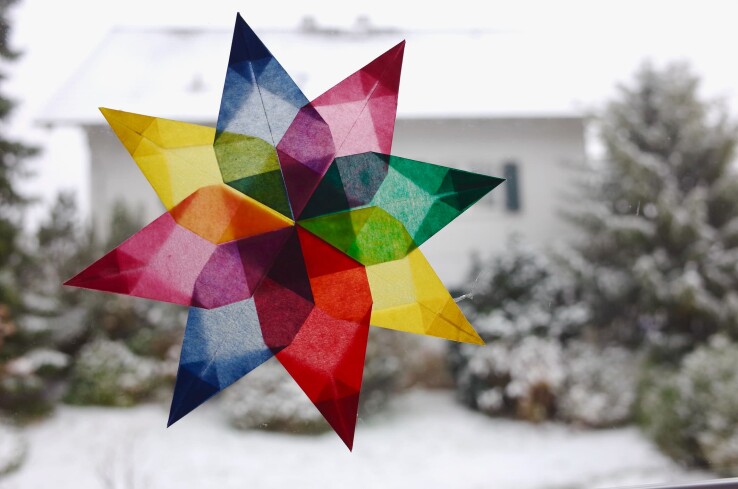 Fenêtre de l’Avent avec une étoile colorée en papier transparent devant un jardin enneigé.