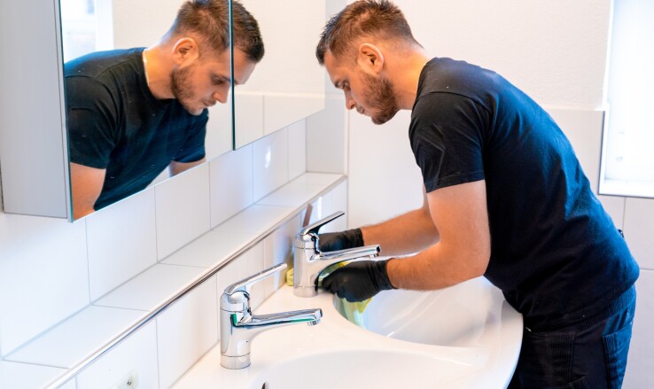 Un homme nettoie un lavabo dans la salle de bains à l'aide d'un chiffon.