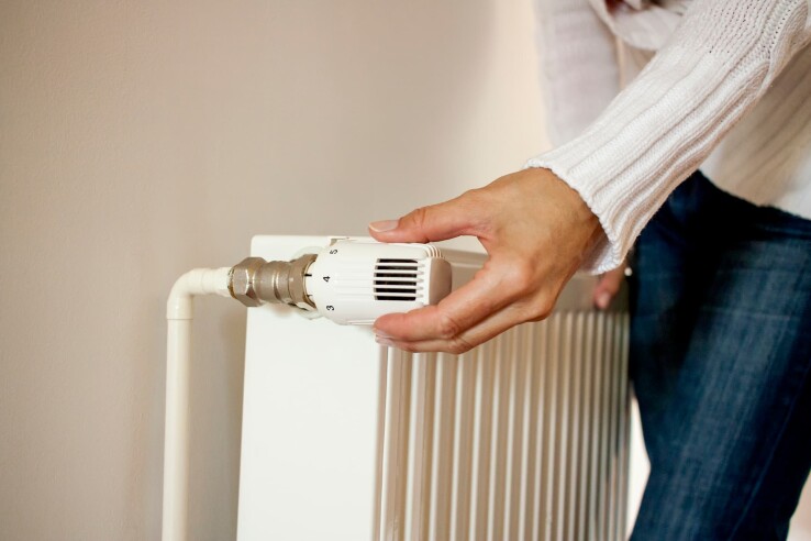 Une personne règle le thermostat d'un radiateur pour faire des économies de chauffage.