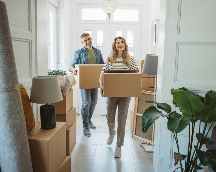 Un couple transporte des cartons de déménagement dans un appartement lumineux – image symbolique illustrant le changement de logement, l'organisation d'un déménagement et la liste de contrôle.