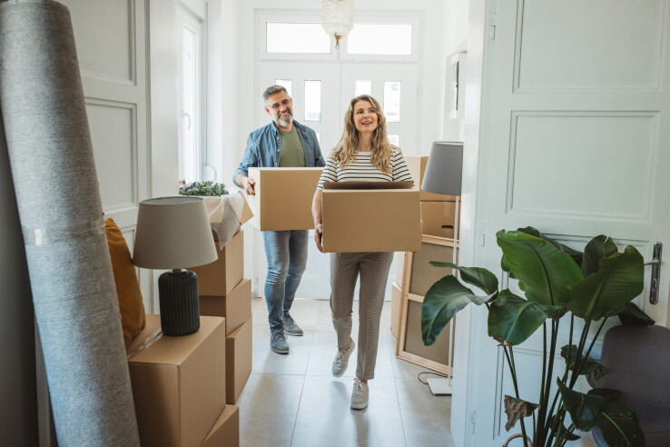 Un couple transporte des cartons de déménagement dans un appartement lumineux – image symbolique illustrant le changement de logement, l'organisation d'un déménagement et la liste de contrôle.
