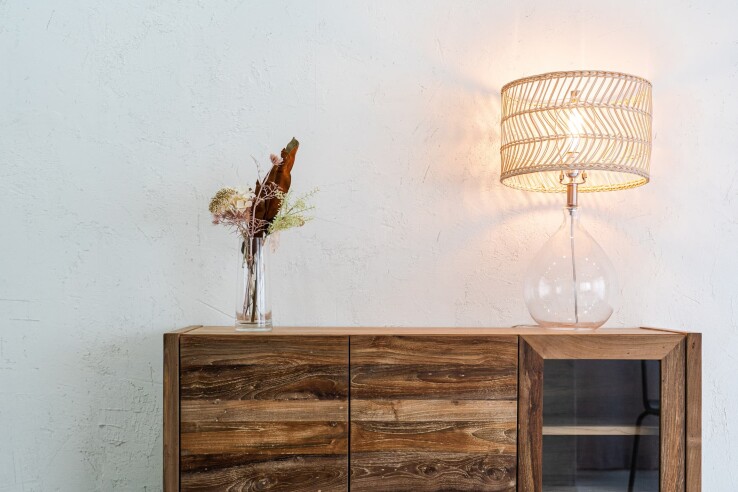 Une commode en bois accompagnée d'une lampe de table décorative et de matériaux naturels dans un salon moderne.