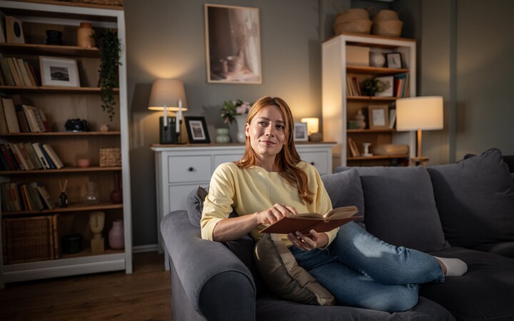 Une femme est assise sur un canapé dans un salon aménagé avec goût, un livre à la main.