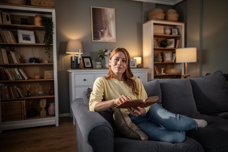 Une femme est assise sur un canapé dans un salon aménagé avec goût, un livre à la main.