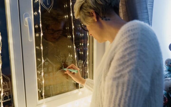 Une personne dessine des motifs de Noël sur une fenêtre de l'Avent à l'aide d'un crayon à craie.