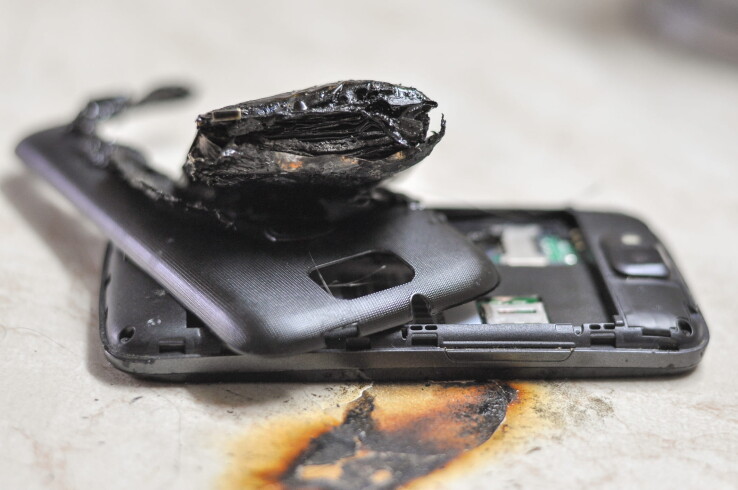 Batterie lithium-ion endommagée dans un smartphone à la suite d'un incendie, présentant un gonflement et des traces de carbonisation.
