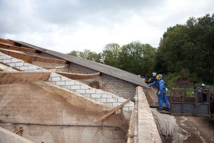 Fachperson in Schutzkleidung bei der Asbestsanierung eines älteren Gebäudedachs mit asbesthaltigen Bauteilen.