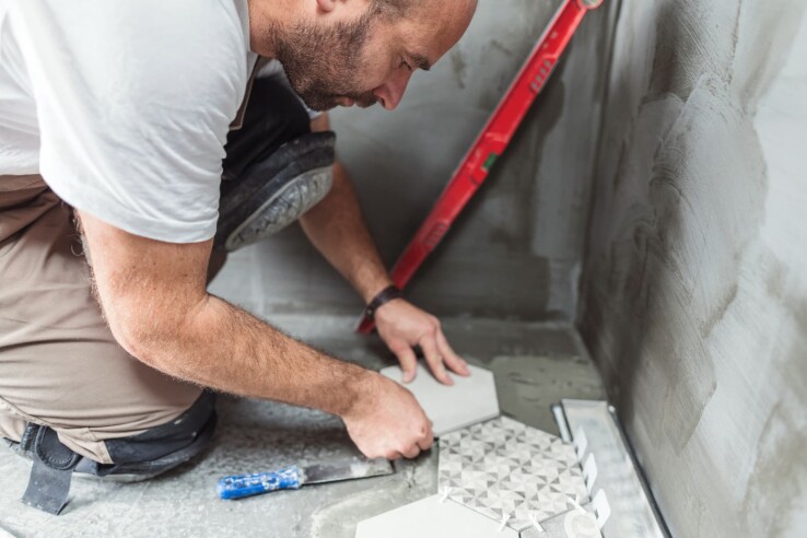 Un homme pose du carrelage pendant les travaux de rénovation de la salle de bains