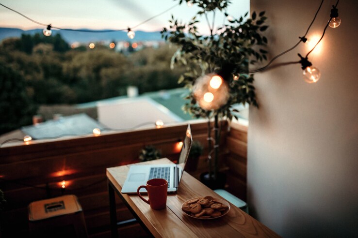 Stimmungsvoll beleuchteter Balkon mit Lichterkette, Tisch, Laptop und Blick ins Grüne.