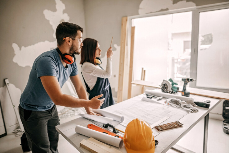 Un couple planifie des travaux de rénovation à l'aide de plans et discute de la gestion du chantier sur place.