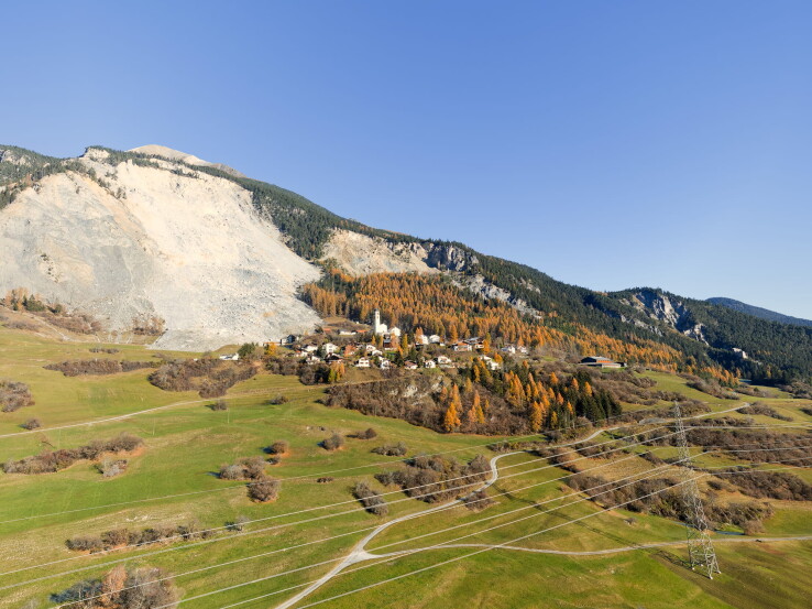 Éboulement au-dessus d'un village dans les Alpes suisses, avec un important cône de débris sur le versant de la montagne.