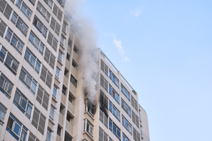 De la fumée s'échappe d'une fenêtre d'un immeuble de plusieurs étages – image symbolique de la prévention des incendies dans les immeubles de grande taille et les immeubles collectifs.