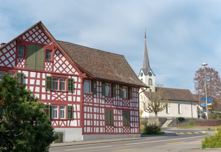 Une maison à colombages historique située à côté d'une église, illustrant bien les bâtiments classés en Suisse.