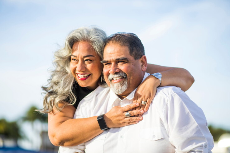 Un couple âgé s'étreint en souriant en plein air, symbolisant ainsi leur union ainsi que la planification successorale commune.