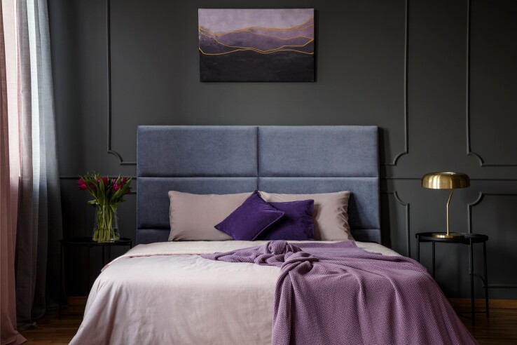 Chambre à coucher avec un mur sombre, un lit rembourré et des textiles violets – le violet est synonyme d'extravagance, de luxe et d'élégance.