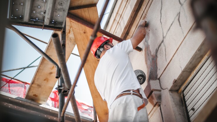 Fachperson saniert die Fassade eines Wohnhauses auf einem Gerüst und bringt eine neue Dämmung an.