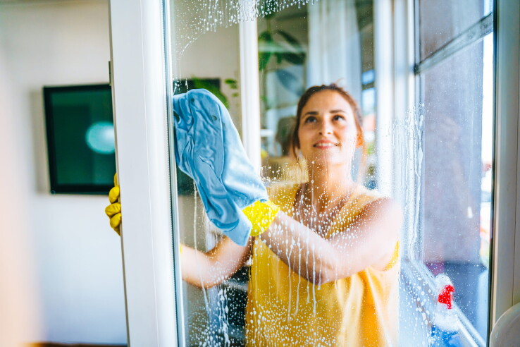 Une femme nettoie ses vitres avec un chiffon en microfibre et de l'eau savonneuse pour obtenir des vitres sans traces.