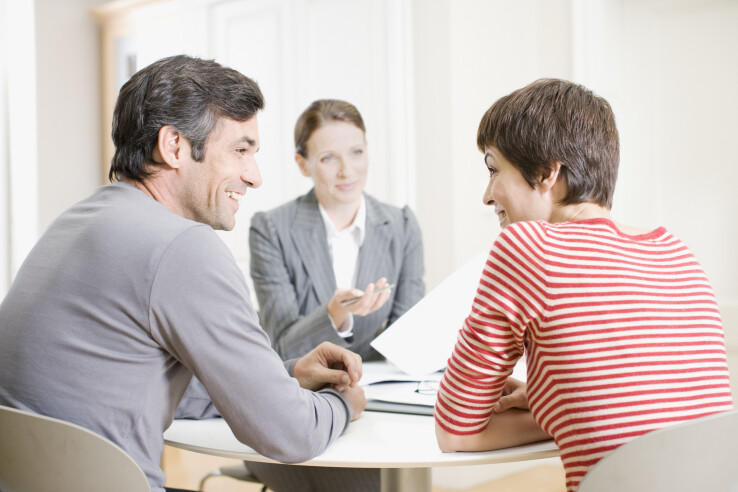 Entretien de conseil entre un couple et une conseillère, illustrant de manière symbolique un financement hypothécaire.