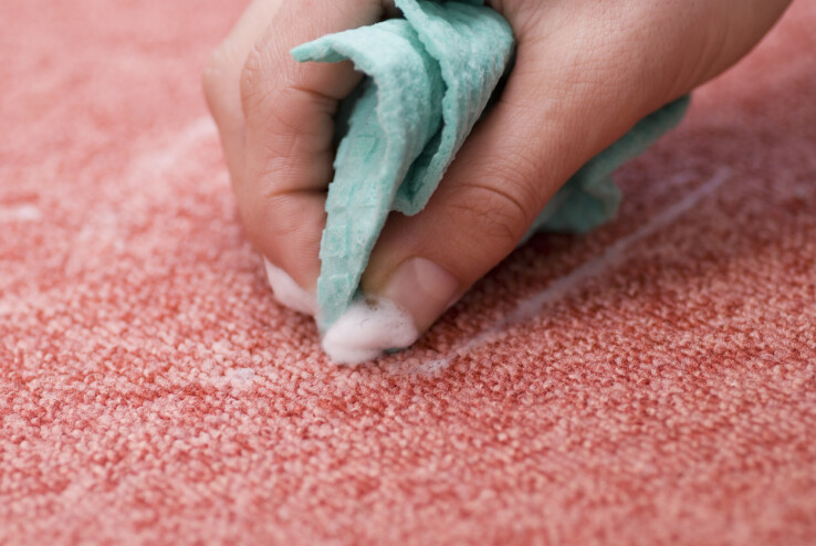 Une main enlève une tache sur un tapis rose à l'aide d'un chiffon.