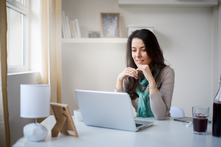 Une femme travaille sur un ordinateur portable dans un bureau à domicile lumineux, avec un bureau bien rangé selon les principes du feng shui.
