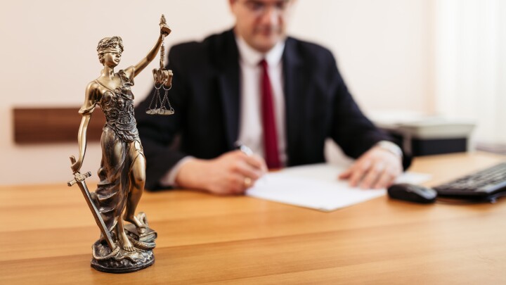 Une statue de Justitia posée sur un bureau, devant une personne qui examine des documents relatifs à un extrait du registre foncier.