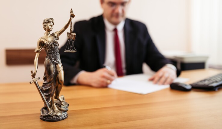 Une statue de Justitia posée sur un bureau, devant une personne qui examine des documents relatifs à un extrait du registre foncier.