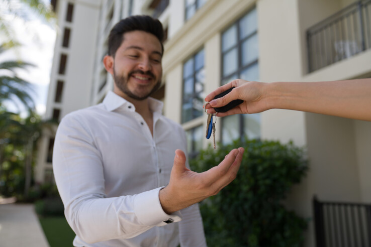 Remise des clés à un jeune homme à l'issue d'un achat immobilier, devant un immeuble résidentiel.