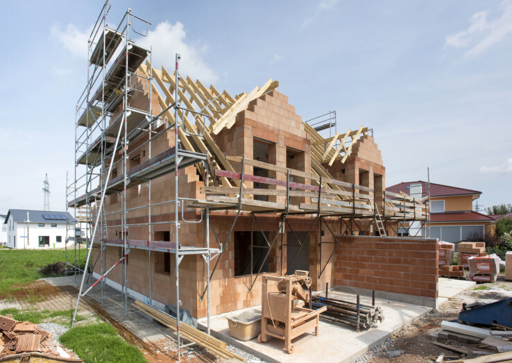 Maison en dur en cours de construction, avec des murs en briques et un échafaudage pendant la phase de construction.