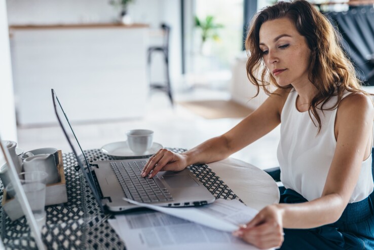 Une femme consulte un contrat hypothécaire sur son ordinateur portable et compare les documents contractuels relatifs à un crédit immobilier.