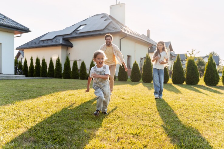 Une famille joue dans le jardin devant une maison individuelle – symbole de l'assurance hypothécaire en Suisse