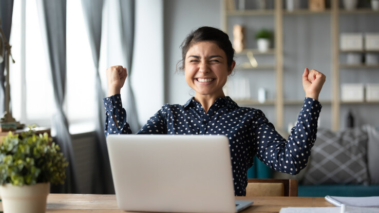 Une femme, devant son ordinateur portable, se réjouit d'avoir réussi à acheter un bien immobilier lors d'une vente aux enchères.