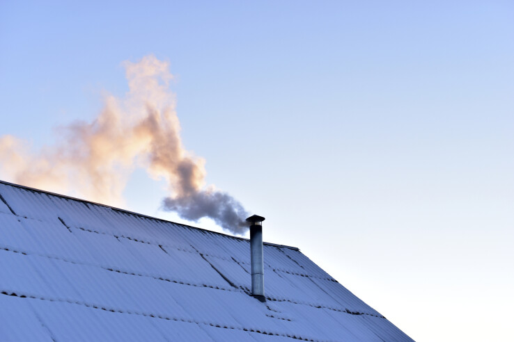 Toit d'une maison recouvert de neige, avec une cheminée d'où s'échappe de la fumée – un ramonage régulier garantit le bon fonctionnement de l'installation de chauffage.