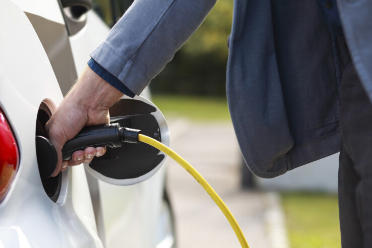 Une main branche le câble de recharge sur une voiture électrique sur le parking d'un immeuble collectif