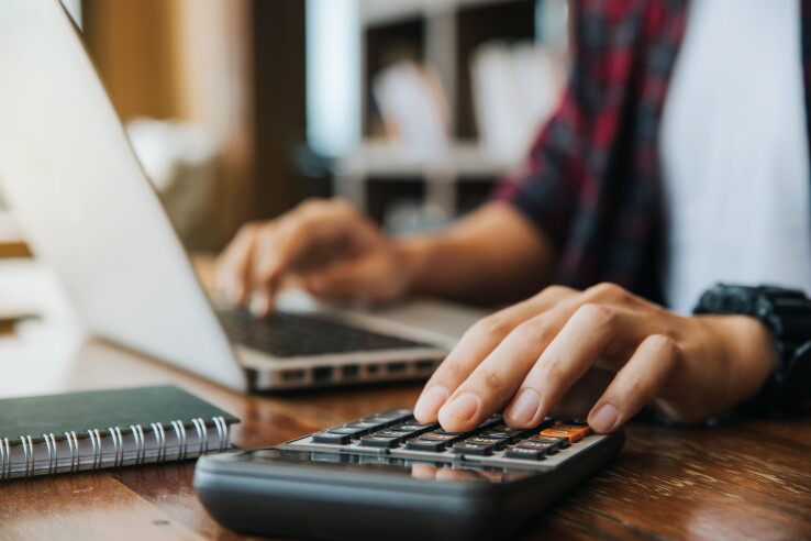 Une personne calcule, à l'aide d'une calculatrice et d'un ordinateur portable, le loyer d'un appartement en Suisse.