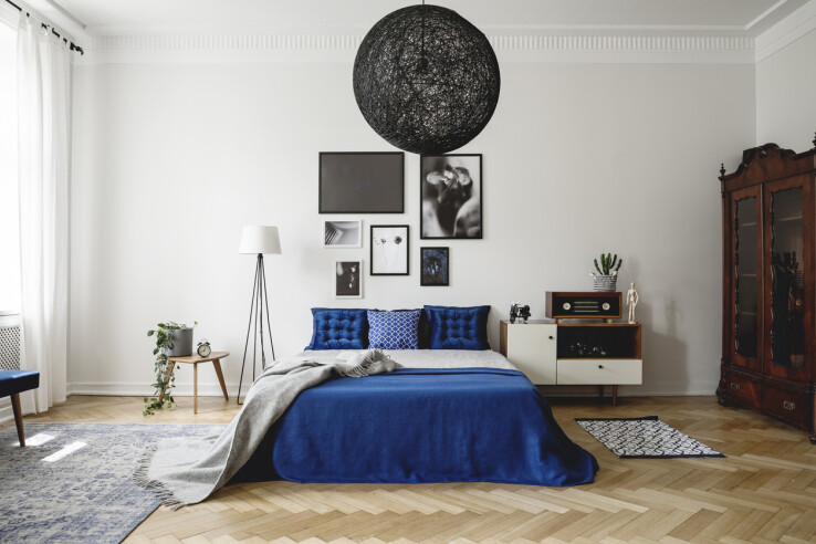 Chambre à coucher avec un lit bleu, une armoire vintage et une commode moderne.