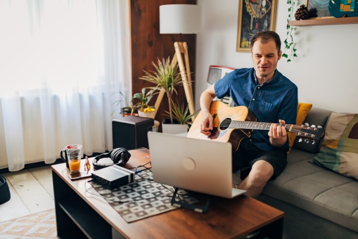Droit locatif et pratique musicale : un homme joue de la guitare dans le salon de son appartement loué et participe à une session en ligne.