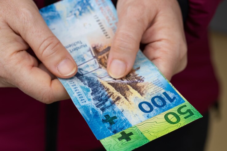 Une personne tient un billet de 100 francs, qui symbolise la différence entre la valeur nominale et la valeur réelle.