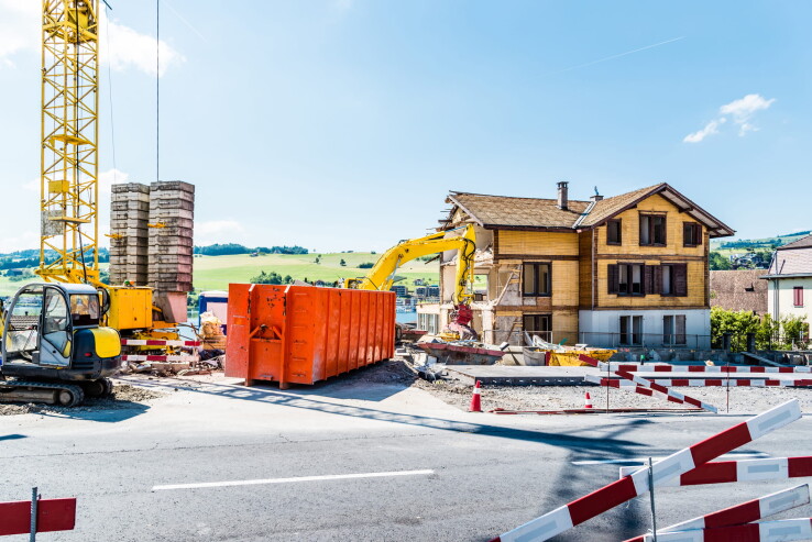 Chantier barricadé devant un immeuble d'habitation, avec des engins de chantier, une grue et des barrières de sécurité.